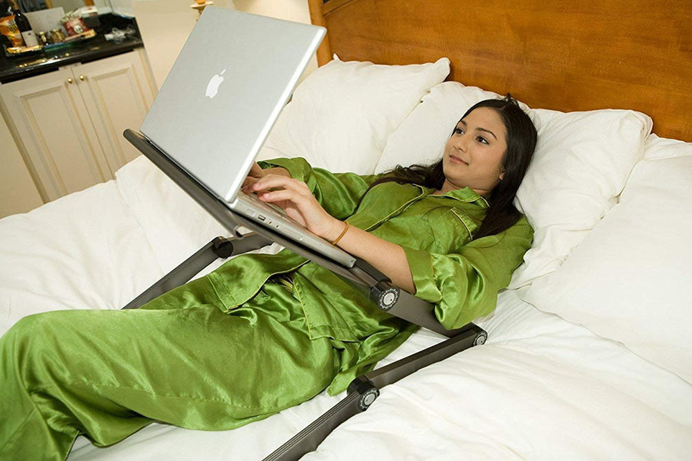 Woman in green pajamas using a laptop on a stand in bed