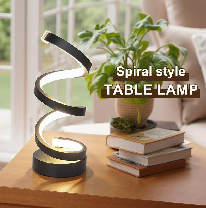 Spiral style table lamp on a wooden surface with books and a plant in the background