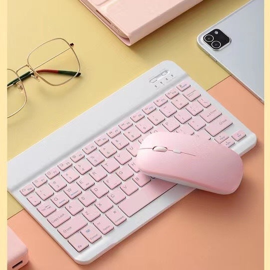 Pink keyboard and mouse set on a colorful desk with glasses and a phone.