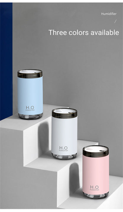 Three cylindrical humidifiers in blue, white, and pink on a geometric shelf with 'H.O' branding.