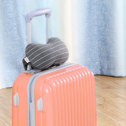 Gray striped neck pillow on a pink suitcase with a light blue curtain background