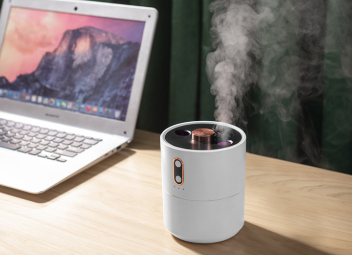 Small white device emitting steam on a wooden surface next to a laptop