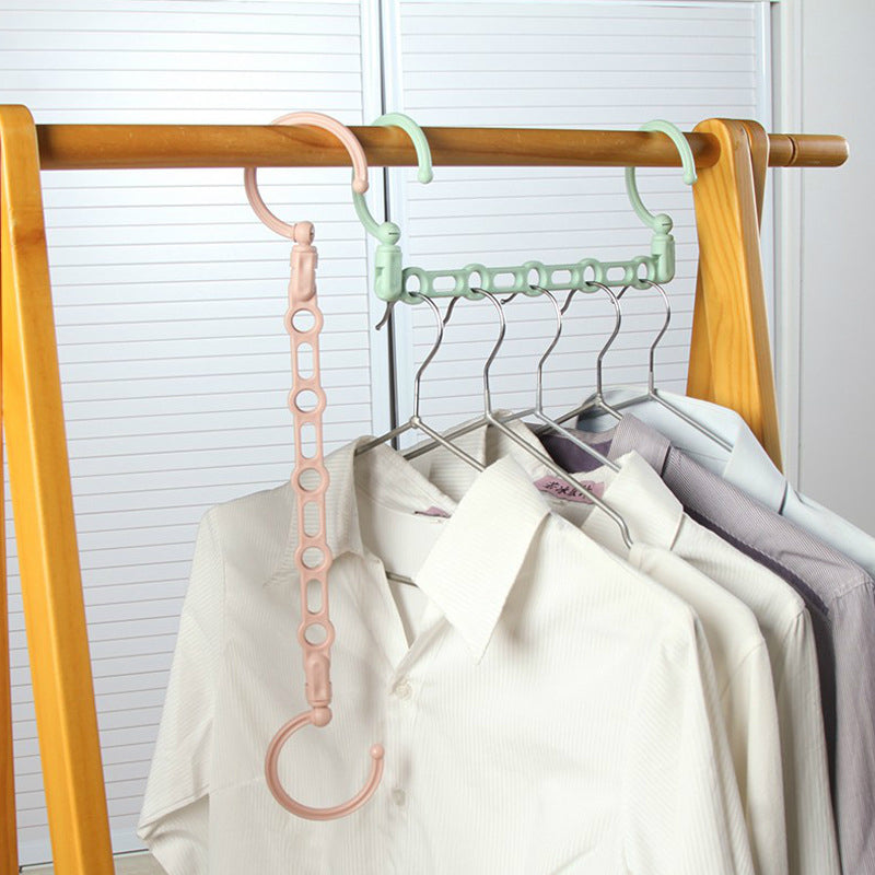 Multi-layered hanger with pink and green hooks on a wooden rack with clothes.