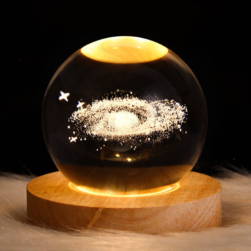 Glass sphere with star and moon design on a wooden base against a dark background