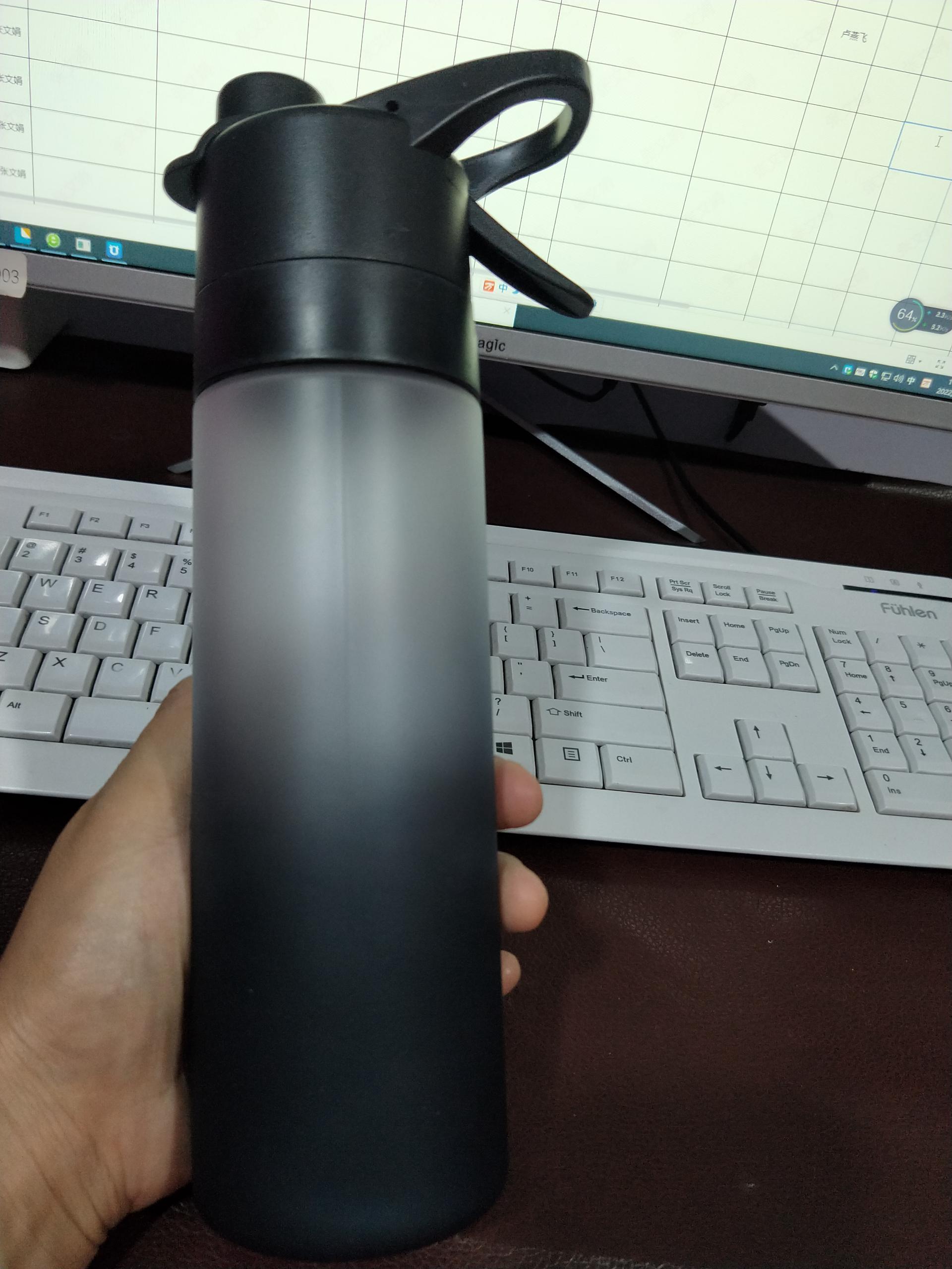 Black water bottle held in front of a computer keyboard on a desk