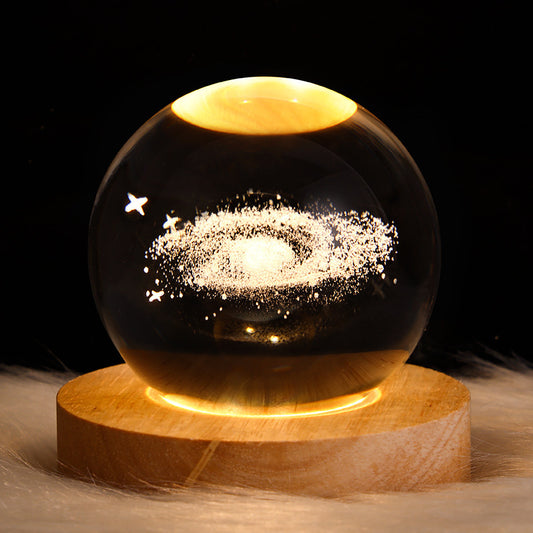 Glass sphere with star and moon design on a wooden base against a dark background