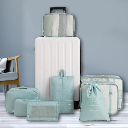 Set of green packing cubes and a white suitcase on a light gray surface with a blue wall background.