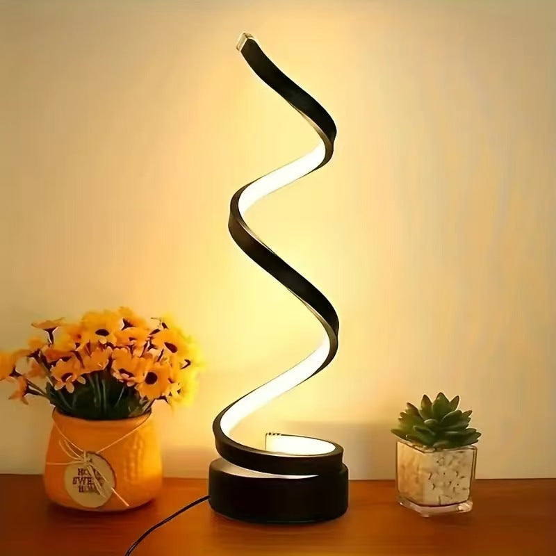 Spiral LED lamp on a wooden surface with decorative plants and flowers.
