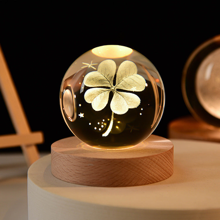 Glass sphere with a four-leaf clover design on a wooden base against a dark background
